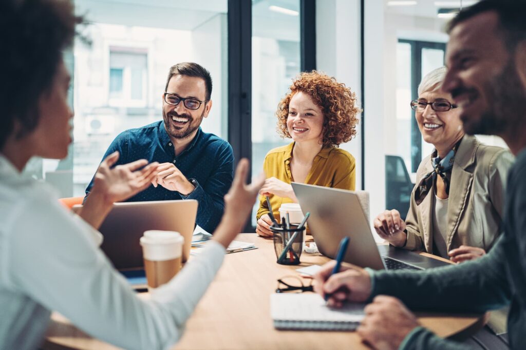 Campaign migration - A group of people sit around a table in an office, discussing with laptops and coffee cups on the table.